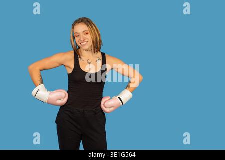 Frau lächelt und steht mit Boxhandschuhen vor blauem Hintergrund Stockfoto