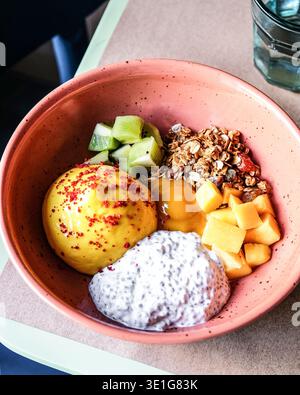 Frische Tropische Früchte Und Knusprige Toppings In Stilvollem Keramikbehälter Neben Wasser Stockfoto