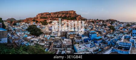 Panoramablick auf das massive Mehrangarh Fort, das auf einer Klippe steht und die weitläufige Blaue Stadt Jodhpur im sanften Licht der Dämmerung überblickt. Stockfoto