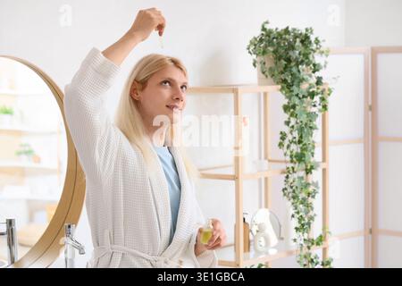 Junger blonder Mann, der Haarserum im Badezimmer aufträgt Stockfoto