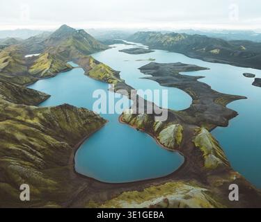 Aus der Vogelperspektive schlängelt sich das türkisfarbene Wasser durch die zerklüftete vulkanische Landschaft, wo dunkle Erde unter dem weichen, ätherischen Himmel Skaftárh auf grünes Moos trifft Stockfoto