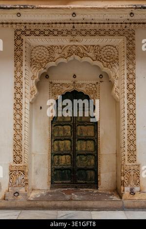 Eine verzierte Steintür mit komplizierten Blumenschnitzereien umgibt eine verwitterte grüne Holztür im Mehrangarh Fort in Jodhpur. Stockfoto