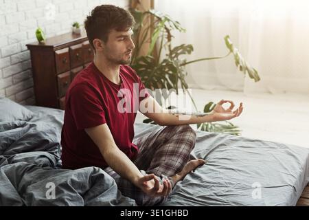 Junger Mann sitzt im Bett in Lotusposition Stockfoto