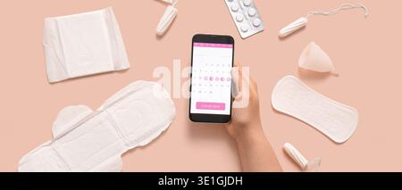 Weibliche Hand mit Menstruationskalender auf dem Bildschirm des Mobiltelefons und verschiedenen Hygieneprodukten für Frauen auf beigefarbenem Hintergrund Stockfoto