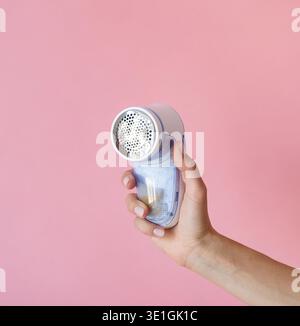 Gerät zum Rasieren von Pellets Kleidung. Rasierer aus Anti-Plush-Gewebe. Elektrischer tragbarer Pullover Pill Defuzzer. Handhalterung und rosafarbener Hintergrund Stockfoto