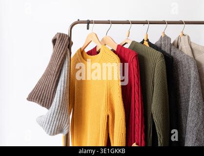 Eine Reihe von verschiedenen farbenfrohen Strickpullis hängt an Kleiderbügeln, weißem Hintergrund, Herbst und Winter Stockfoto