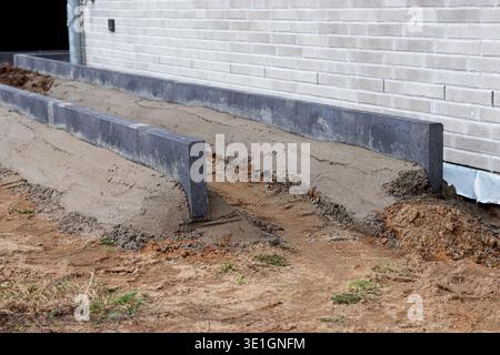 Betongründungsformen auf sandigem Boden neben einer Ziegelmauer, die für das Gießen von Beton in einem Wohnbauprojekt bereit sind Stockfoto