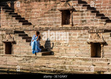 Eine junge Frau sitzt auf den breiten Sandsteinvorsprüngen des Toorji Ka Jhalra Steppbrunnen in Jodhpur mit Blick auf das tiefe Wasser des alten Stausees. Stockfoto