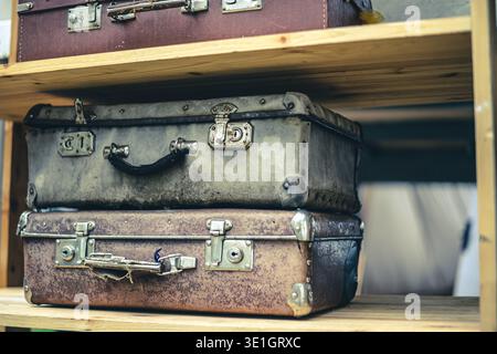 Mehrere alte alte Koffer liegen auf einem Holzregal übereinander. Vintage-Nietgriffe und mechanische Schlösser. Alte verblasste Haut. Hochwertige Pho Stockfoto