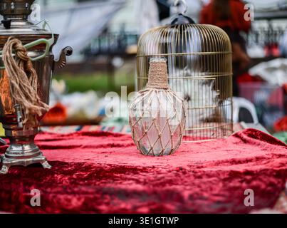 Auf der roten Tischdecke befinden sich eine Vintage-Flasche, ein Samovar und ein Vogelkäfig. Tauschen Sie alte Antiquitäten und Vintage-Artikel aus. Hochwertige Fotos Stockfoto