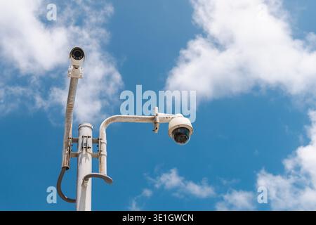 Sicherheitsüberwachungskameras auf Metallpfosten gegen blauen Himmel mit Wolken Stockfoto
