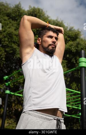 Junger athletischer Mann, der sich vor dem Training in einem Park ausdehnt. Gesunder Lebensstil, Outdoor-Fitnesstraining und Aufwärmroutine in einer natürlichen Umgebung. Stockfoto