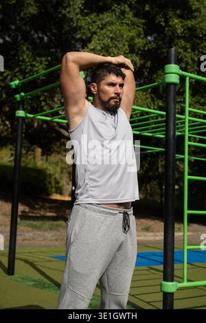 Junger athletischer Mann, der sich vor dem Training in einem Park ausdehnt. Gesunder Lebensstil, Outdoor-Fitnesstraining und Aufwärmroutine in einer natürlichen Umgebung. Stockfoto