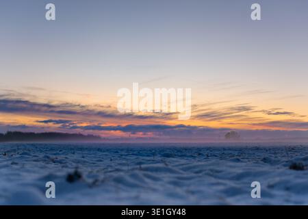 Winterabendlandschaft mit schneebedecktem Feld und orangen Wolken, die die untergehende Sonne am Horizont verbergen. Hochwertige Fotos Stockfoto