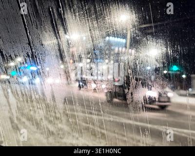 Die Autos fahren nachts schnell durch die Stadt, während die Lichter leuchten und ein nebeliges Fenster unschärfen lässt. Stockfoto