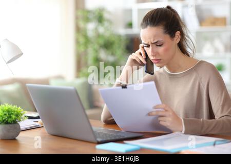 Besorgte Selbstständige, die online arbeiten und telefonisch über Papierdokumente sprechen Stockfoto