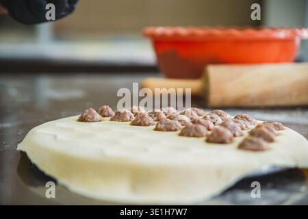 Nahaufnahme eines Tisches mit rohem Teig, auf dem kleine Bällchen Hackfleisch gelegt sind, fertig zum Kochen von Knödeln. Vorrichtung zur schnellen Herstellung von Knödeln Stockfoto