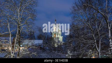 Durch die Zweige von Bäumen bedeckt mit Schnee schöne weiße Kirche mit Beleuchtung im Winter am Abend. Hochwertige Fotos Stockfoto