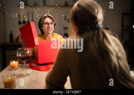 Paare mittleren Alters feiern Valentinstag mit romantischem Abendessen zu Hause und tauschen Geschenke aus. Valentinstag-Konzept Stockfoto
