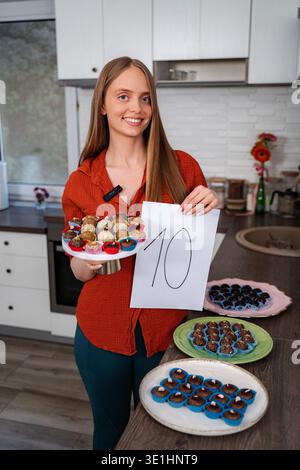 Lächelnde Frau, die Nummer zehn mit vielen Desserts hält Stockfoto