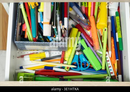Unordentliche offene Schublade voller farbenfroher Schulpapiere und Bleistifte. Stockfoto