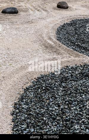 Zen-Garten mit gemarkten Sandmustern und schwarzen Kiessteinen, die eine minimalistische Landschaftskomposition im botanischen Garten von Cascate di Varone T schaffen Stockfoto