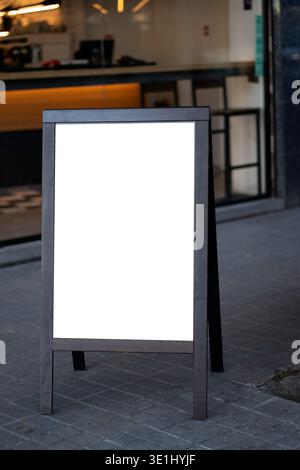 Leeres Holzrahmenschild auf dem Bürgersteig, das Kunden zu einem Café-Eingang lockt und ein Menü oder eine spezielle Werbebotschaft in der städtischen Straßenumgebung anbietet Stockfoto