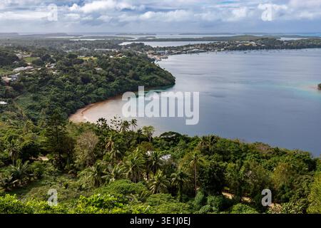 Ein Panoramablick auf eine Küstenstadt, eingebettet zwischen üppigen grünen Hügeln und mit Blick auf eine ruhige blaue Bucht mit Segelbooten. Die Szene fängt die Sache ein Stockfoto