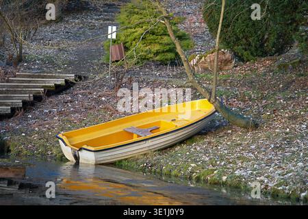 Ein gelb-weißes Kunststoff-Vergnügen- und Fischerboot, das am Ufer eines Stausees vor Anker liegt. Hochwertige Fotos Stockfoto