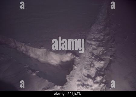 Frische Fußabdrücke in tiefem Schnee in einer ruhigen Winternacht, beleuchtet durch dunkle Lichter der Stadt. Die kalte atmosphärische Szene spiegelt das Winterwetter wider, menschlich Stockfoto