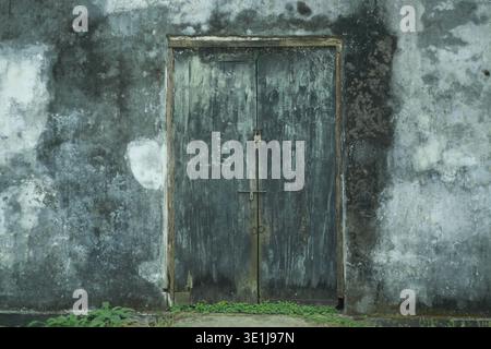 Alte Holztür an einer verwitterten Betonwand mit rustikaler Textur im Freien Stockfoto