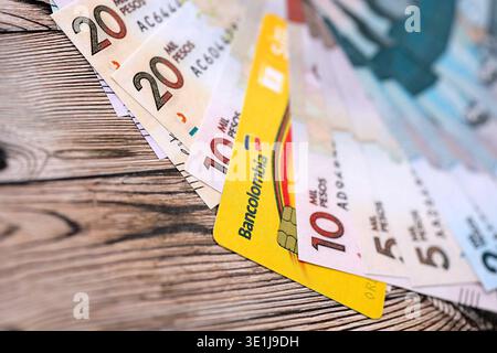 KIEW, UKRAINE - 28. JANUAR 2026 Bankolombienkarte und kolumbianische Peso-Geldscheine auf dem Tisch in Nahaufnahme. Bancolombia ist die beliebteste Bank in Kolumbien Stockfoto