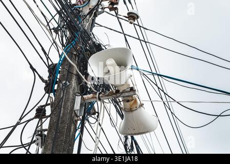 Lautsprecher an Versorgungsmasten mit verwickelten elektrischen Leitungen in Thailand montiert Stockfoto