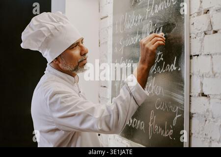 Mann mittleren Alters unterrichtet Kochkurs und schreibt Menü auf Blackboard Stockfoto