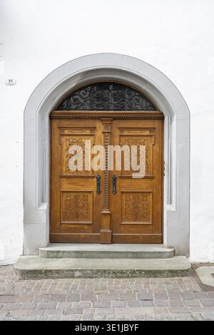 Frontalblick auf ein historisches Portal an einer Fassade des alten Stadthauses mit einer zweiflügeligen Holztür mit komplizierten Schnitzereien und Blumenornamenten im Barock Stockfoto