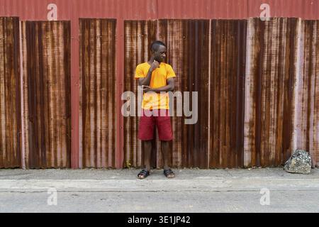 Jungen schwarzen afrikanischen Mann denken und nach unten schaut, während man gegen die alten rostigen Blech Wand Stockfoto