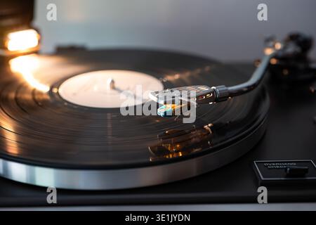Nahaufnahme eines Schallplattenspielers mit einem Stift auf einer rotierenden schwarzen Vinylscheibe, hervorgehoben durch sanfte Beleuchtung, die die Eleganz des Plattenspielers unterstreicht Stockfoto