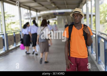 Junge schwarze afrikanische touristische Mann und denken an die Fußgängerbrücke mit der U-Bahn Station in Bangkok, Thailand Stockfoto