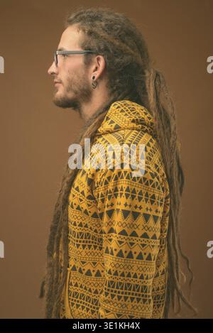 Studio shot von jungen hübschen Hispanic Mann mit Dreadlocks tragen Hoodie gegen braunen Hintergrund Stockfoto