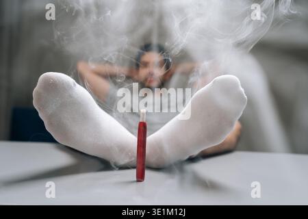 Mann, der sich mit Füßen in weißen Socken auf dem Tisch entspannt und dicken Rauch von elektronischen Zigaretten erzeugt. Konzepte von Komfort, Freizeit, alternativem Rauchen Stockfoto
