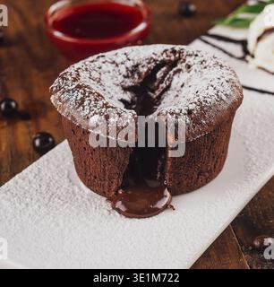 Schokoladen-Lavakuchen mit geschmolzener Schokolade auf einem weißen Teller, serviert mit einer Schaufel Vanilleeis, Beeren und Schokoladenstückchen Stockfoto
