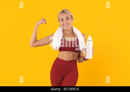 Frau, die Muskeln zeigt und Wasserflasche in Workout-Kleidung auf gelbem Hintergrund hält Stockfoto