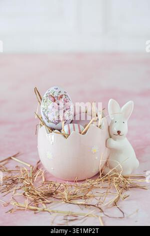 Osterdekoration mit einem Porzellanhase und Ei, gefüllt mit dekorativen rosa und lila ostereiern auf rosa Hintergrund, vertikal mit Kopie Spac Stockfoto