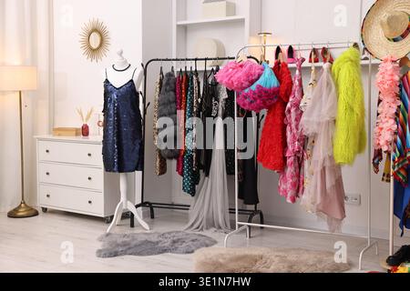 Verschiedene festliche Kleidung hängt an Regalen und weibliche Schaufensterpuppe in der Nähe der weißen Wand im Ankleidezimmer Stockfoto