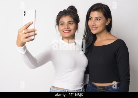 Studio-Aufnahme von zwei jungen schönen persischen Frauen zusammen als Schwestern vor weißem Hintergrund Stockfoto