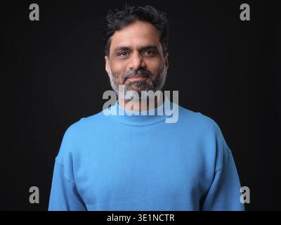 Studioaufnahme eines reifen hübschen bärtigen indischen Mannes mit lockigen Haaren vor schwarzem Hintergrund Stockfoto