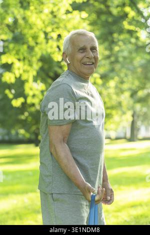 Aktiver älterer Mann, der während seines Fitnesstrainings mit einem Gummiwiderstandsband im grünen Stadtpark trainiert Stockfoto