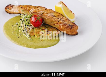 Köstlich gegrilltes Lachsfilet, serviert mit einer lebendigen grünen Sauce, Zitrone und frischer Beilage Stockfoto