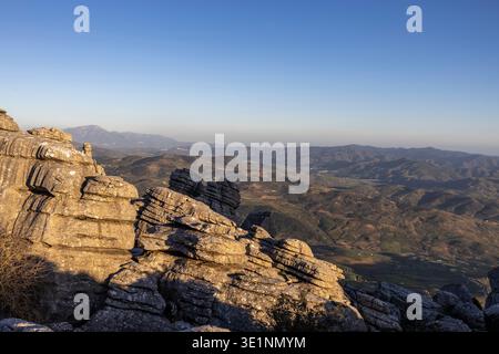 Besucher wandern durch einzigartige Felsformationen in El Torcal in Spanien. Die Sonne untergeht über den Hügeln, schafft Schatten und hebt die Landschaft hervor. Dies ist Stockfoto