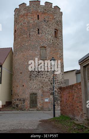 Kopfsteinpflaster-Straßenszene in einer kleinen Stadt in Deutschland mit historischen Gebäuden und einem mittelalterlichen Turm im Hintergrund, vertikales Format. Stockfoto